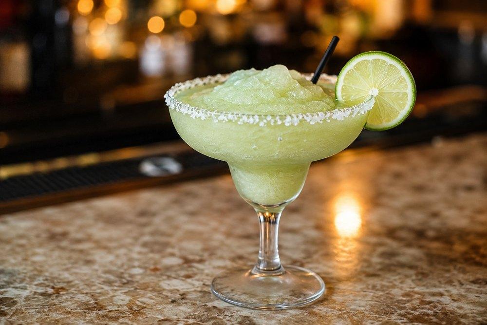 Frozen Margarita jako světle zelená ledová tříšť v koktejlové sklenici se solí na okraji a plátkem limetky.