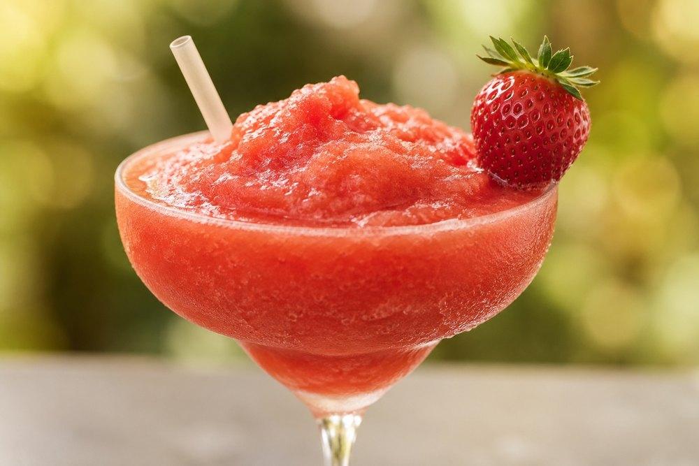 Jahodová frozen Margarita jako sytě růžová ledová tříšť v koktejlové sklenici, ozdobená čerstvou jahodou.